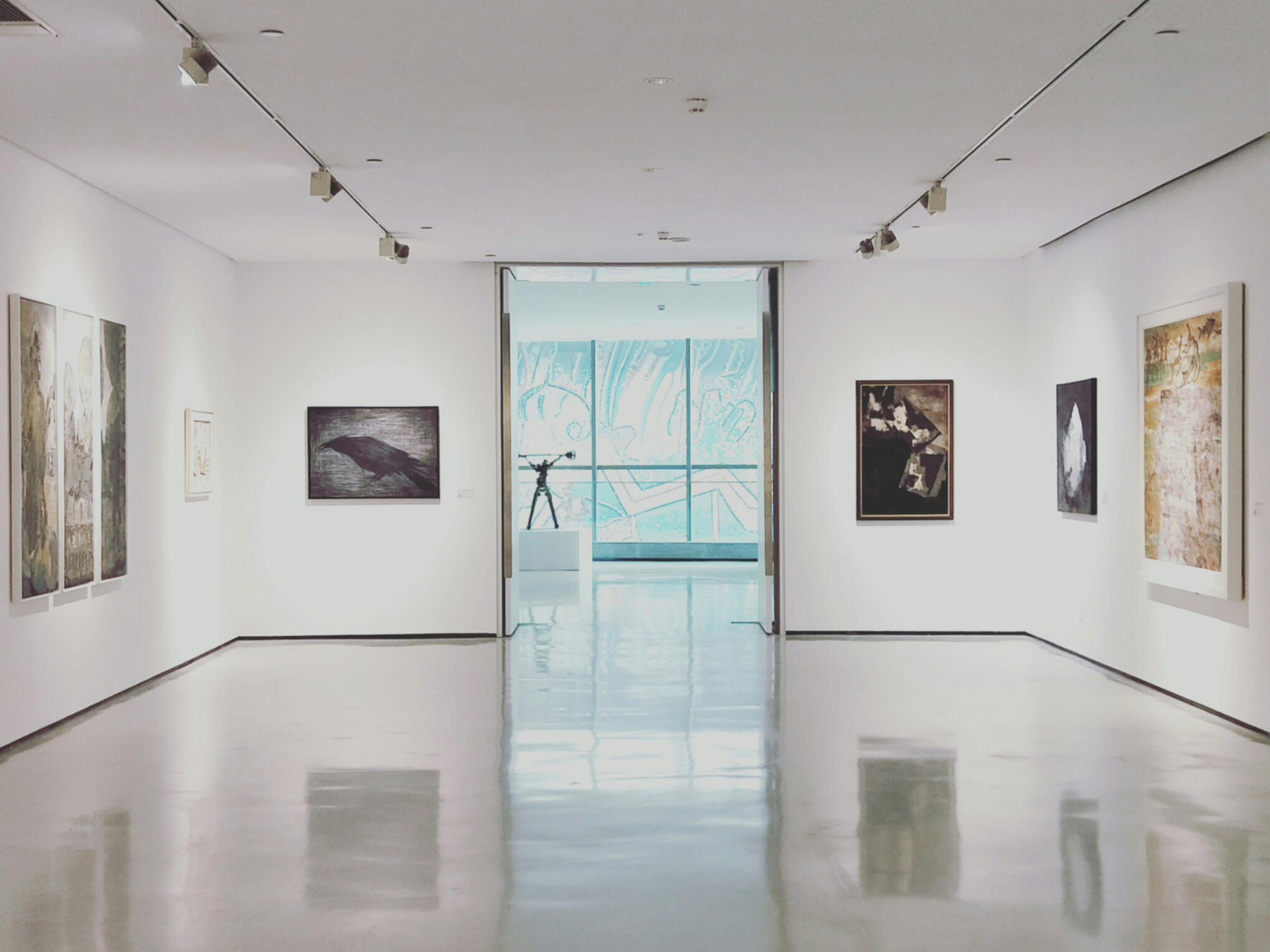 A quiet contemporary art gallery with framed artworks, polished floors and a glass doorway.